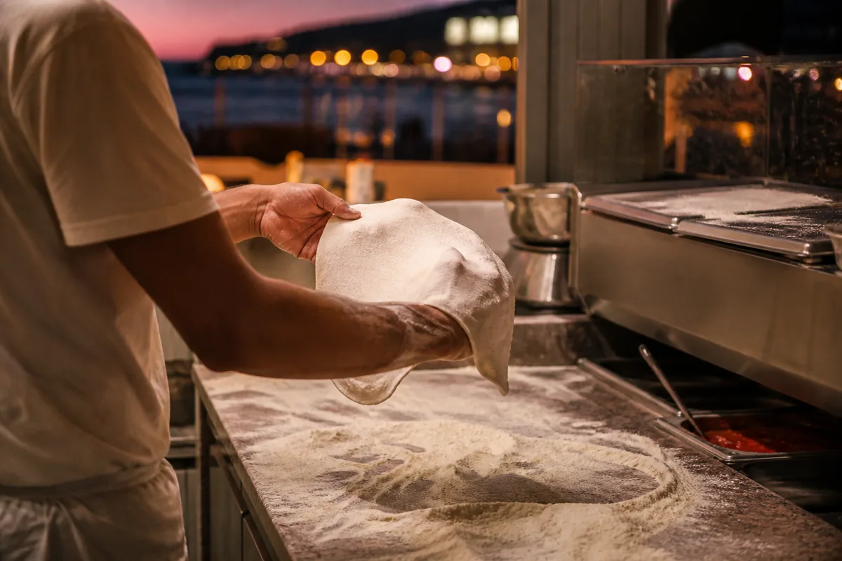 Pizzaiolo étirant une pâte à pizza sur un plan de travail fariné dans une cuisine de bord de mer